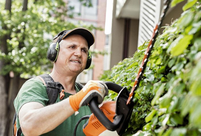 Mann mit Ohrschutz schneidet Hecke mit Gerät