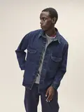 Männliches Model im dunklem Denimlook mit einer Jeansjacke und darunter einem grauen Oberteil