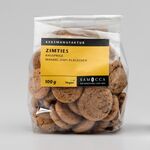 Braune Kekse in einer Klarsichtverpackung. Gelb-schwarzes Etikett mit der Kennzeichnung "Keksmanufaktur", "vegan", "Zimties knuspriche Mandel-Zimt Plätzchen"