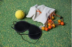 Schlafmaske, gelber Ball, Stoffbeutel und ein Band mit kleinen Glöckchen auf einer grünen Oberfläche.