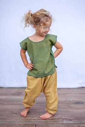 Kleines Mädchen mit einem grünen Kurzarm Top aus Baumwolle und einer grüne Hose stellt ihre Hände an die Hüfte